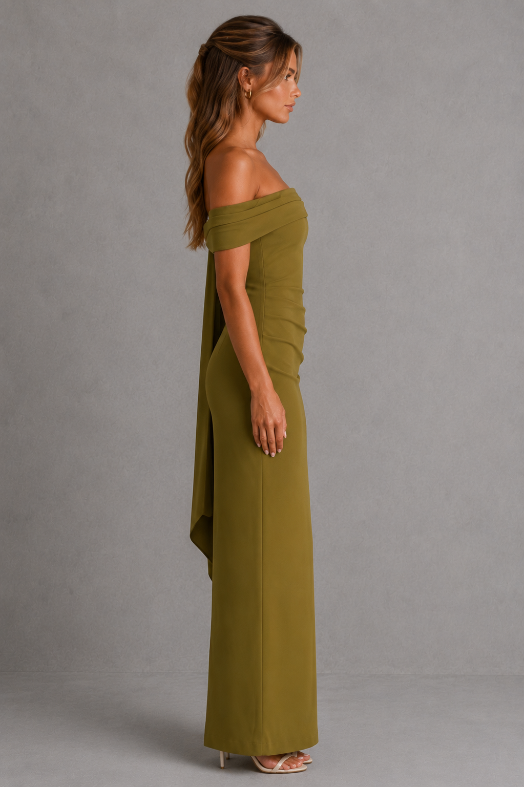 Woman wearing a premium bardot maxi dress with an asymmetric pleated neckline, draped knot shoulder tie, fitted bodice, asymmetric pleated waist, column skirt, and centre back split in structured crepe fabric.