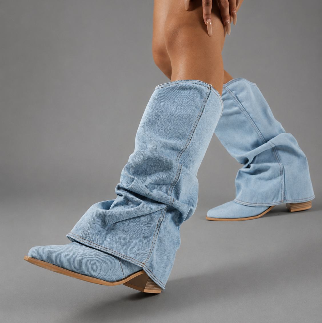 Women’s light blue denim knee-high boots with a ruched shaft, sleek pointed toe, square block heel, and statement denim finish.