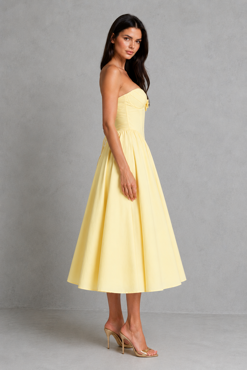 Women's strapless corset midi dress with a sweetheart neckline, pleated cups, bow detail, structured boned bodice, and a full tulle-lined gathered skirt, designed for elegant party and occasion wear.