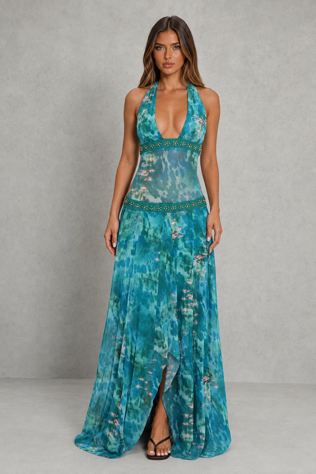 Womenโs halter backless maxi dress with plunging neckline, beaded waist detailing, fitted silhouette, and flowing waterfall hem.