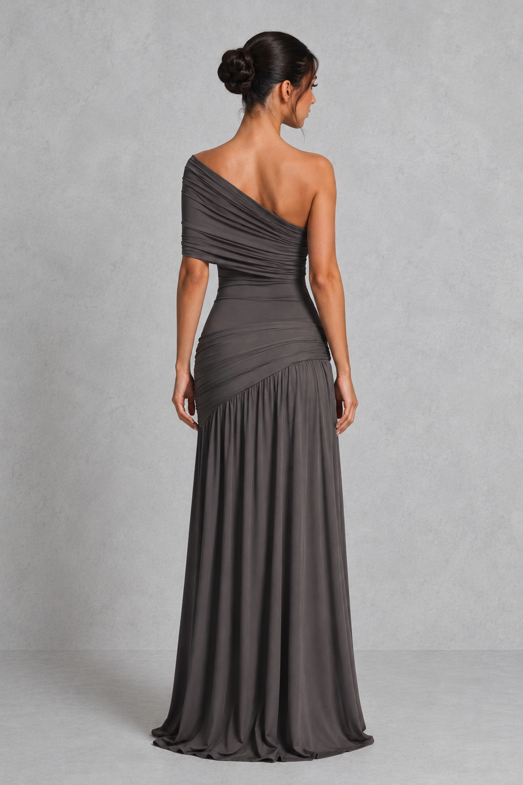 Woman wearing a one-shoulder maxi dress in soft slinky jersey fabric, featuring asymmetric pleating, a draped waist with silver-tone buckle detail, a flowing gathered skirt, and a thigh-high split for an elegant evening look.