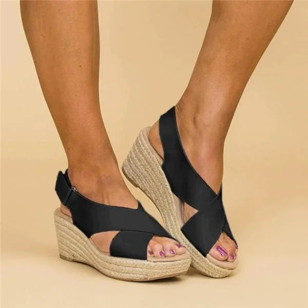 Black wedge sandals with espadrille sole worn by a person on a beige background