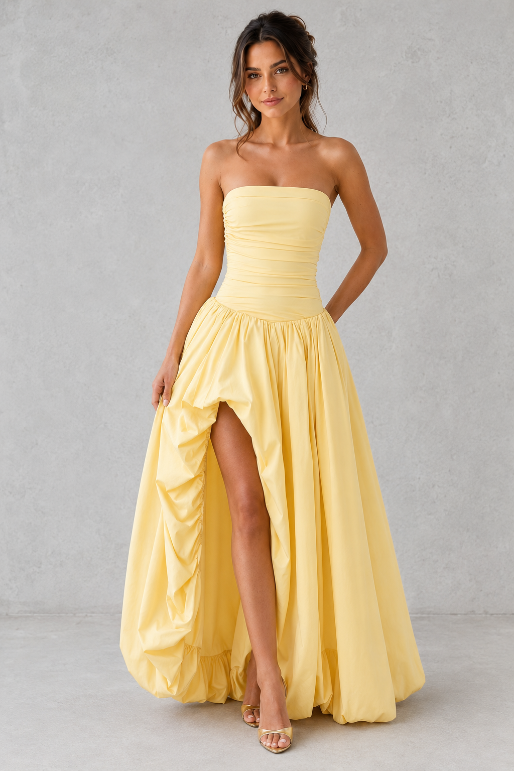 Women's strapless maxi dress with a ruched fitted bodice, dropped waist, lace-up back, dramatic puffball skirt, and thigh-high split, designed for elegant evening events and formal occasions.