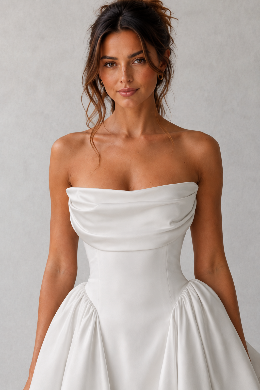 Woman wearing a strapless satin mini dress featuring a softly draped cowl neckline, structured boned bodice, lace-up back, voluminous skirt with pleated godet panels, and a detachable statement bow, ideal for parties, weddings, and special occasions.