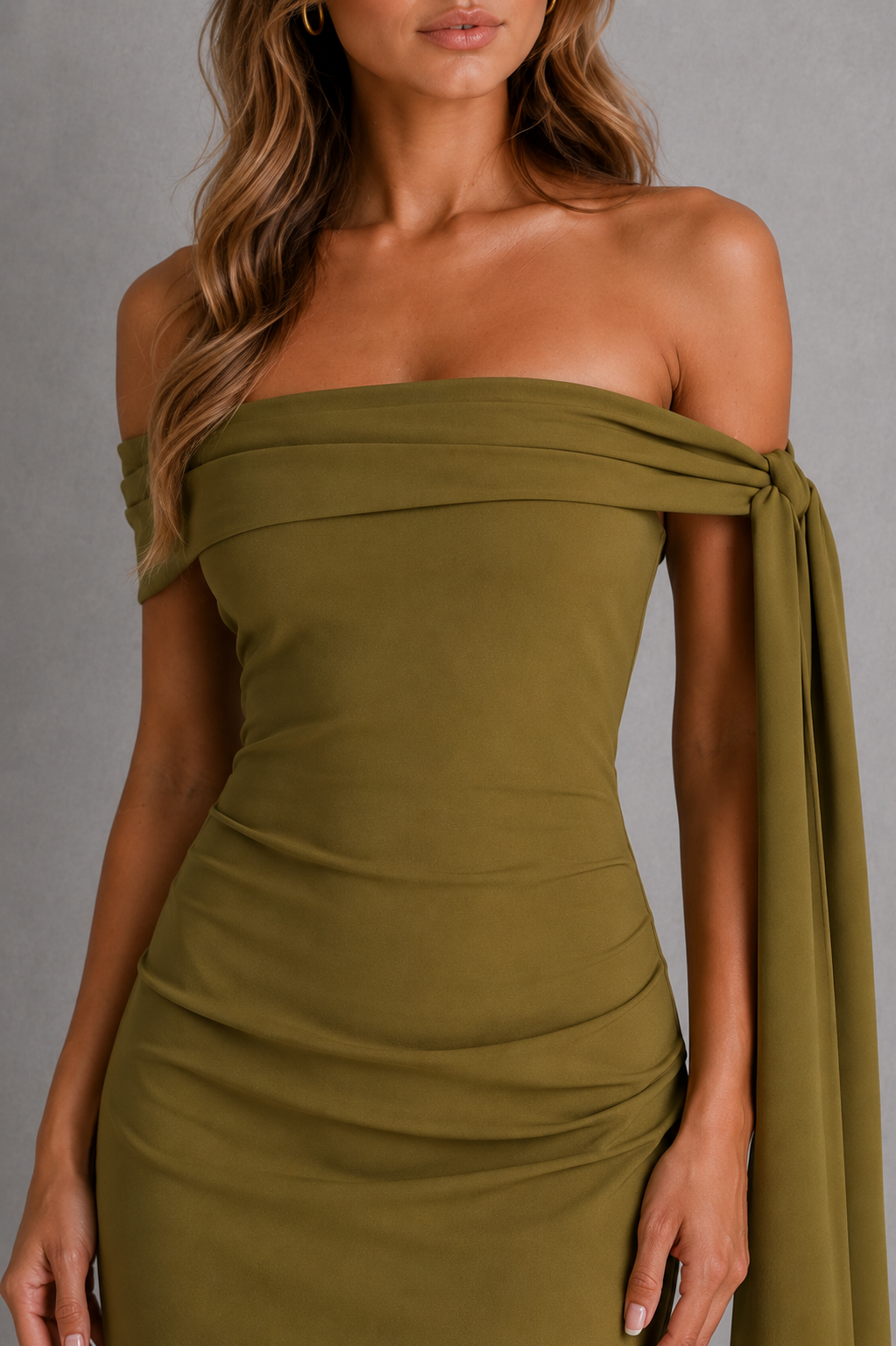 Woman wearing a premium bardot maxi dress with an asymmetric pleated neckline, draped knot shoulder tie, fitted bodice, asymmetric pleated waist, column skirt, and centre back split in structured crepe fabric.