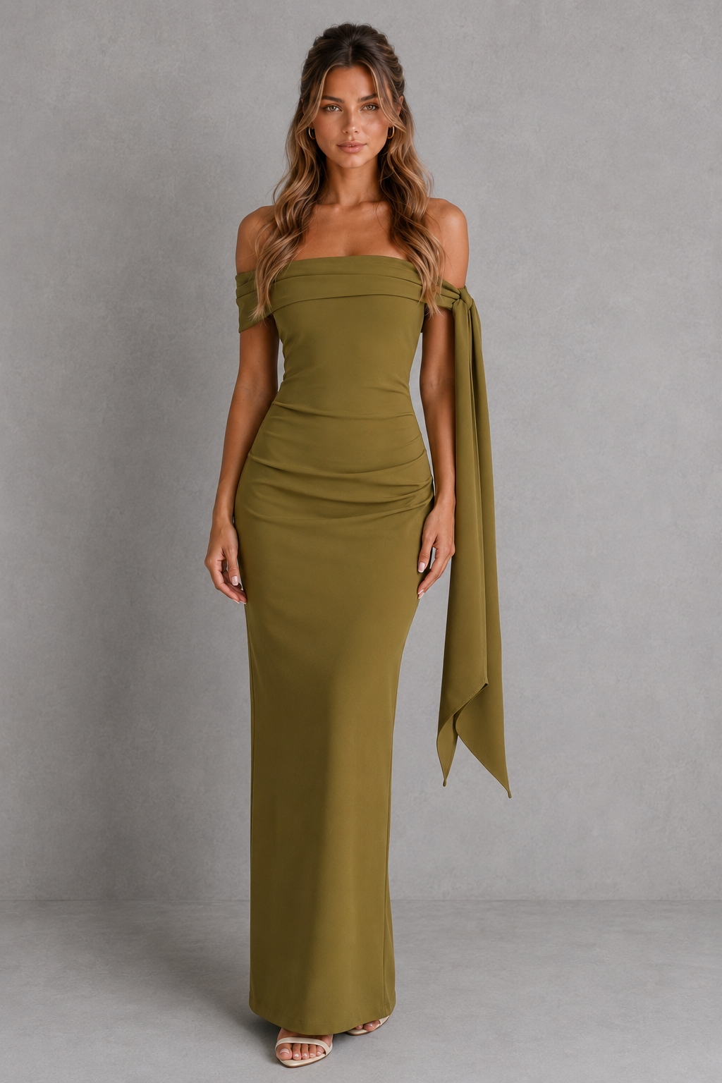 Woman wearing a premium bardot maxi dress with an asymmetric pleated neckline, draped knot shoulder tie, fitted bodice, asymmetric pleated waist, column skirt, and centre back split in structured crepe fabric.