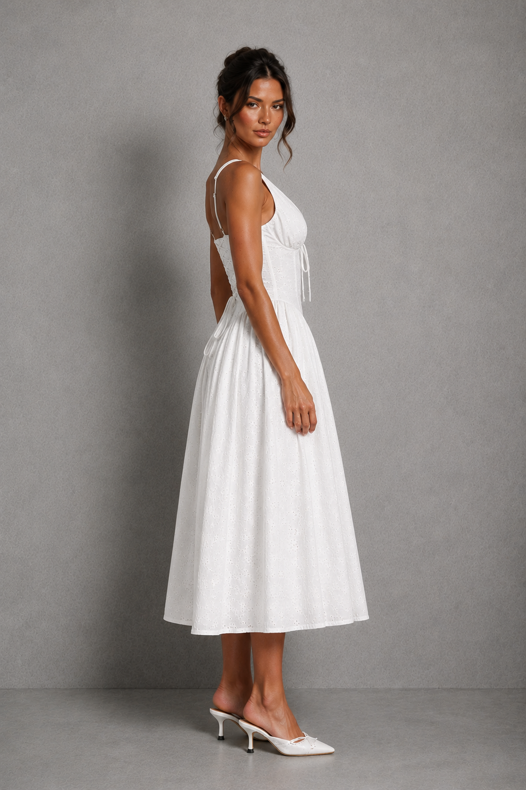 Women’s white broderie anglaise midi dress with plunge neckline, gathered bust, adjustable straps, lace-up back, and flowing godet skirt.