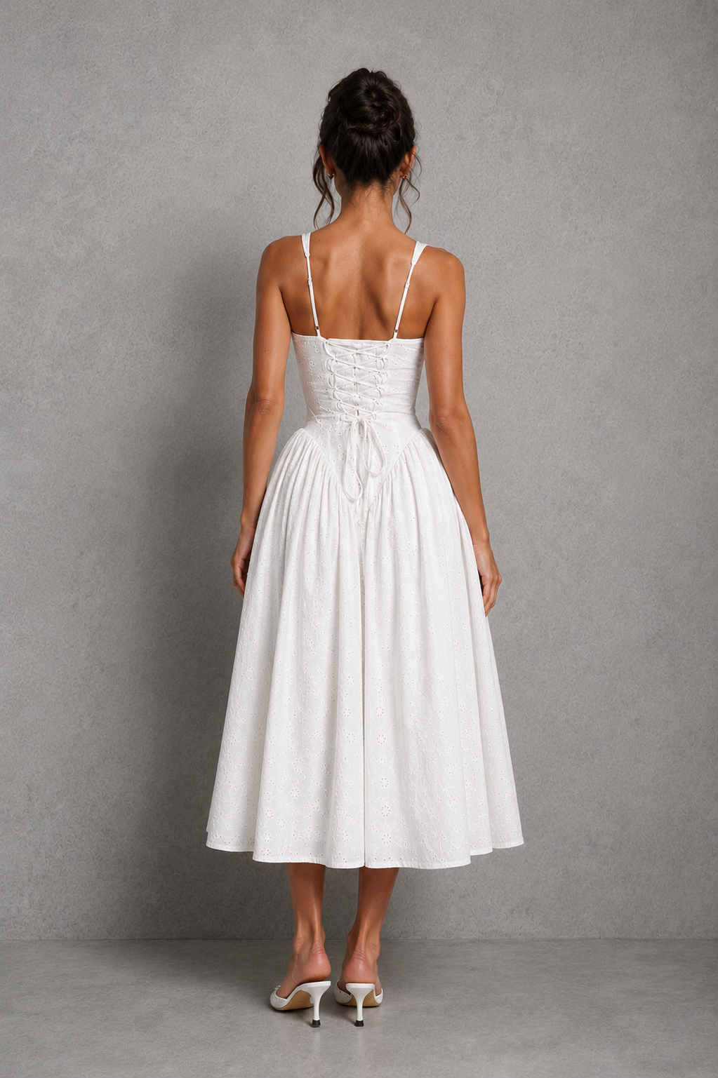 Women’s white broderie anglaise midi dress with plunge neckline, gathered bust, adjustable straps, lace-up back, and flowing godet skirt.
