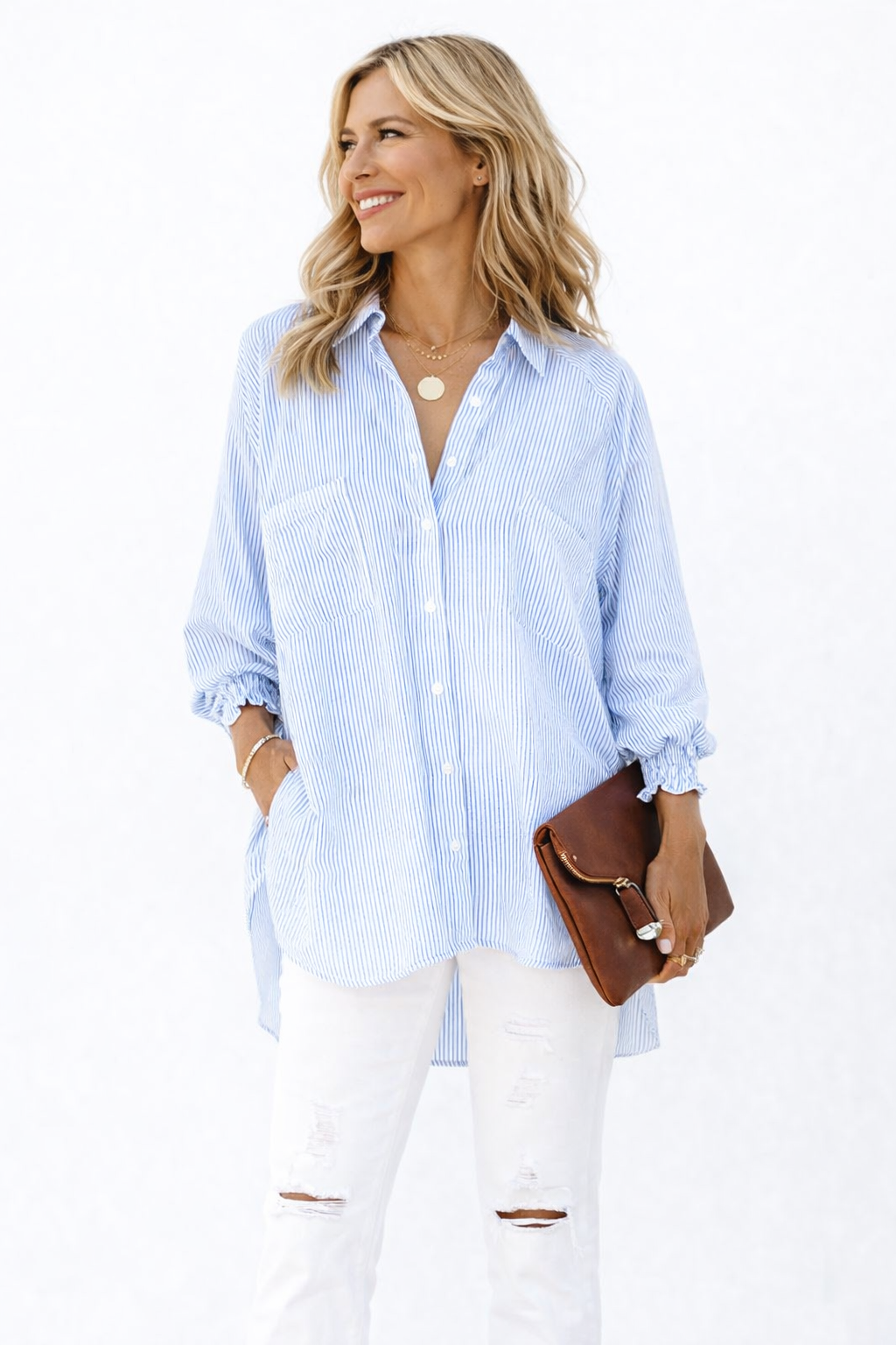 Woman wearing a light blue striped shirt and white pants, holding a brown clutch against a white background