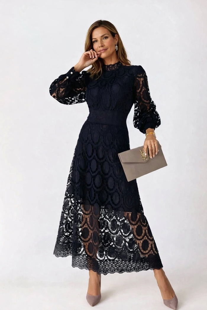 Woman wearing a black lace dress holding a clutch against a white background