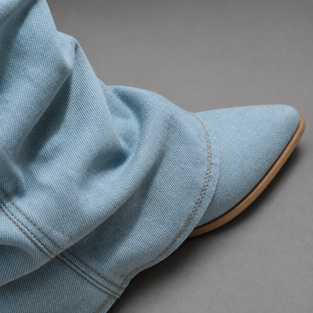 Women’s light blue denim knee-high boots with a ruched shaft, sleek pointed toe, square block heel, and statement denim finish.