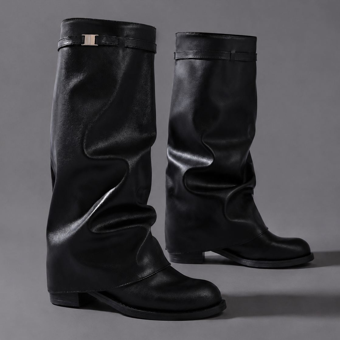 Women’s pointed toe slouch knee-high boots with a relaxed shaft, low block heel, pull-on design, and polished metal cuff detail.