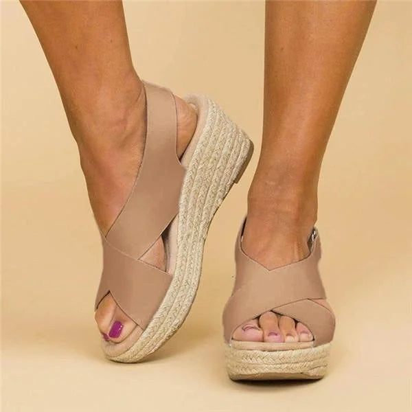 Beige wedge sandals with espadrille sole worn by a person on a beige background