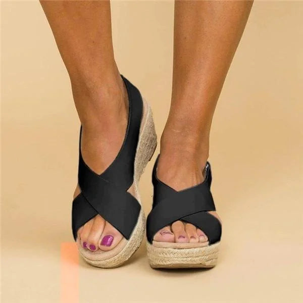 Black wedge sandals with jute sole worn by a person on a beige background