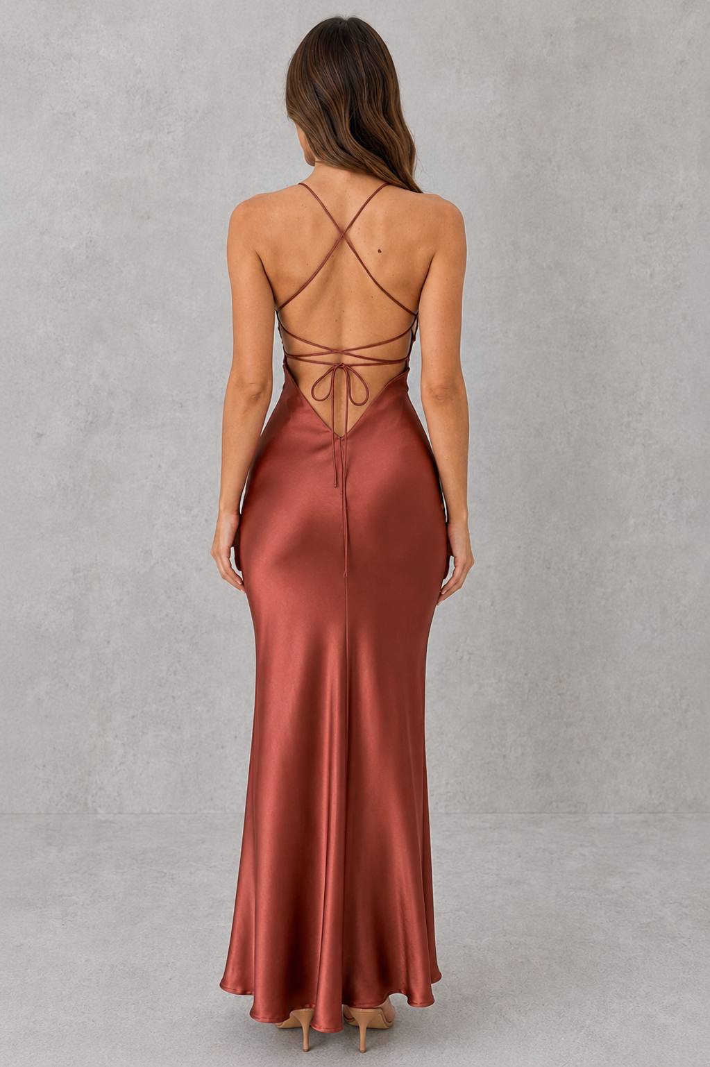 Woman wearing a satin maxi dress with a body-skimming silhouette, delicate shoulder straps, crossover open-back detail, and a floor-length design, styled for formal evening occasions.
