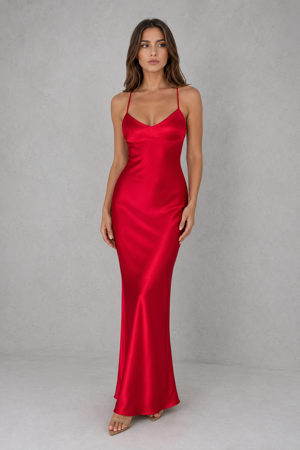 Woman wearing a satin maxi dress with a body-skimming silhouette, delicate shoulder straps, crossover open-back detail, and a floor-length design, styled for formal evening occasions.