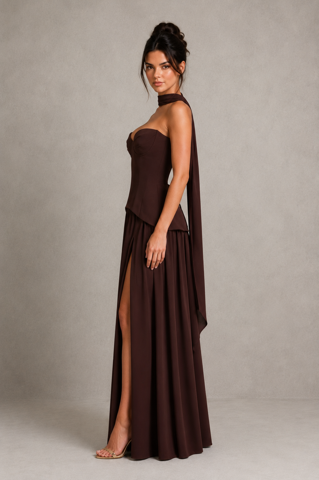 Woman wearing a strapless chiffon maxi dress with a structured corset-inspired bodice, pleated cups, flowing gathered skirt, thigh-high split, and matching chiffon scarf, styled for evening events and formal occasions.