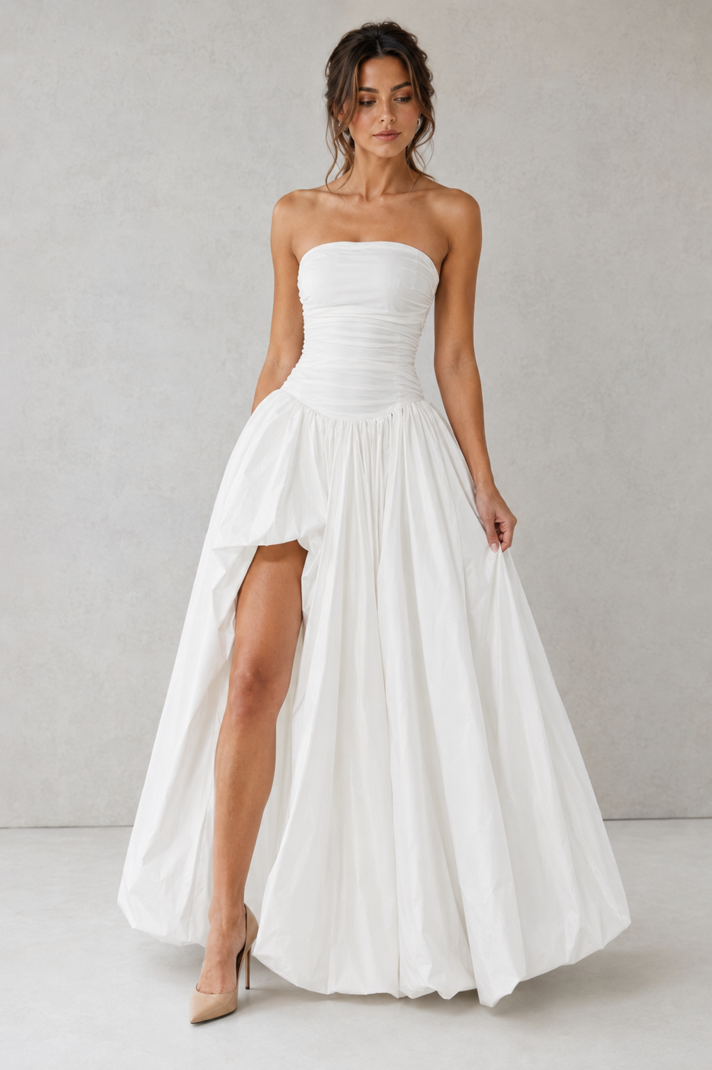 Women's strapless maxi dress with a ruched fitted bodice, dropped waist, lace-up back, dramatic puffball skirt, and thigh-high split, designed for elegant evening events and formal occasions.