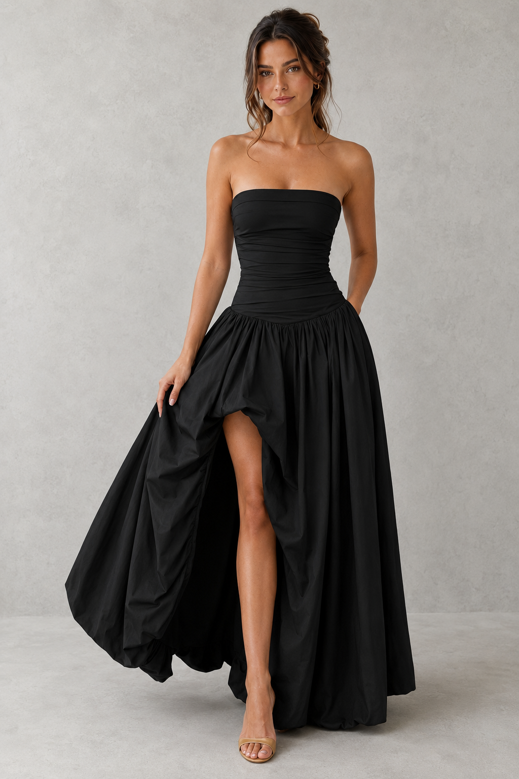 Women's strapless maxi dress with a ruched fitted bodice, dropped waist, lace-up back, dramatic puffball skirt, and thigh-high split, designed for elegant evening events and formal occasions.